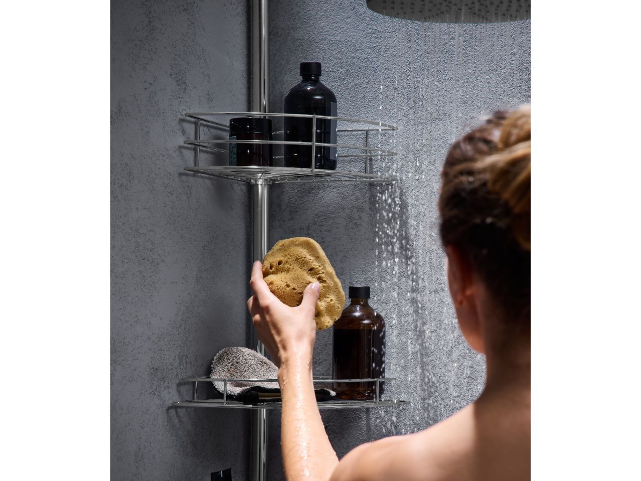 Woman in shower holding a natural sponge, with shower caddy and bottles.