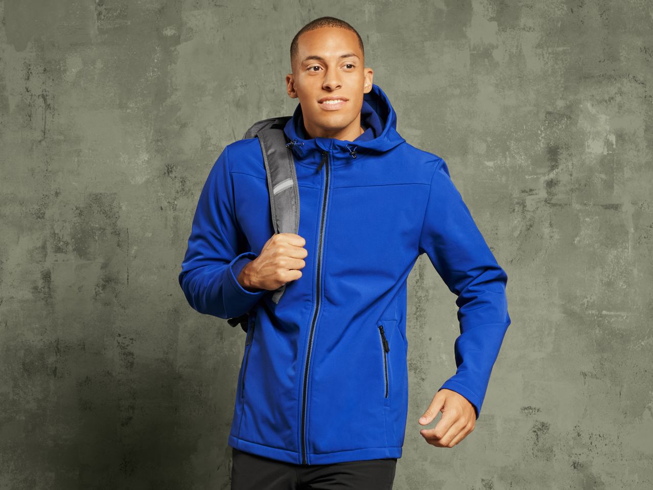 A man in a blue softshell jacket with a backpack looking to the right.