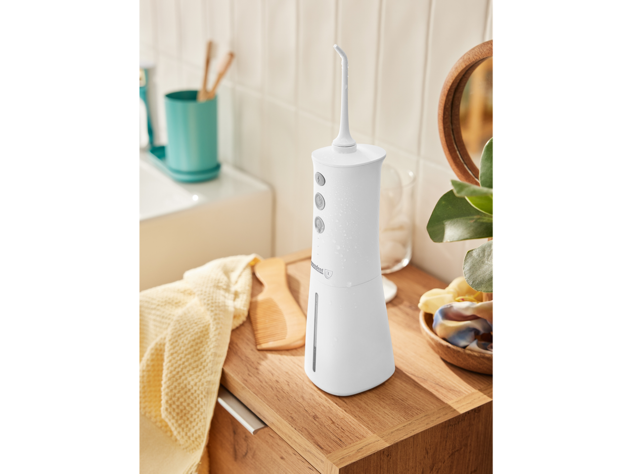 Witte Nevadent monddouche op een houten badkamerkastje met een handdoek.