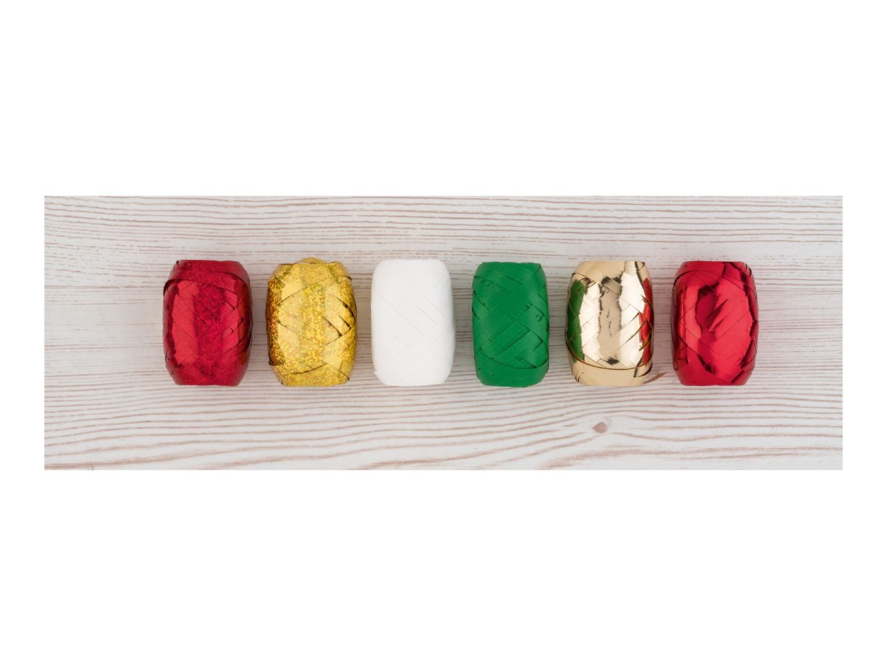 Six spools of curling ribbon in red, gold, white, and green on a wooden surface.