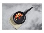 Overhead shot of a black frying pan with cooked shrimp, cherry tomatoes, and garlic on a grey surface.