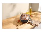 Freshly baked bread in a loaf pan on a wooden cutting board with olive oil and chilies.