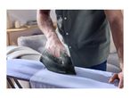 Man ironing a light blue shirt on an ironing board with a dark grey iron.