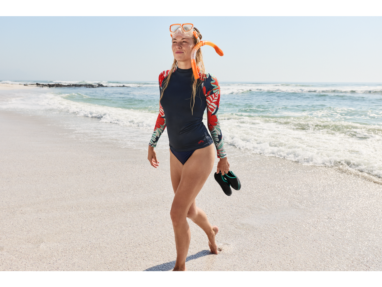 CRIVIT Ladies' Aqua Shoes held by a woman in a rash guard on a sandy beach.