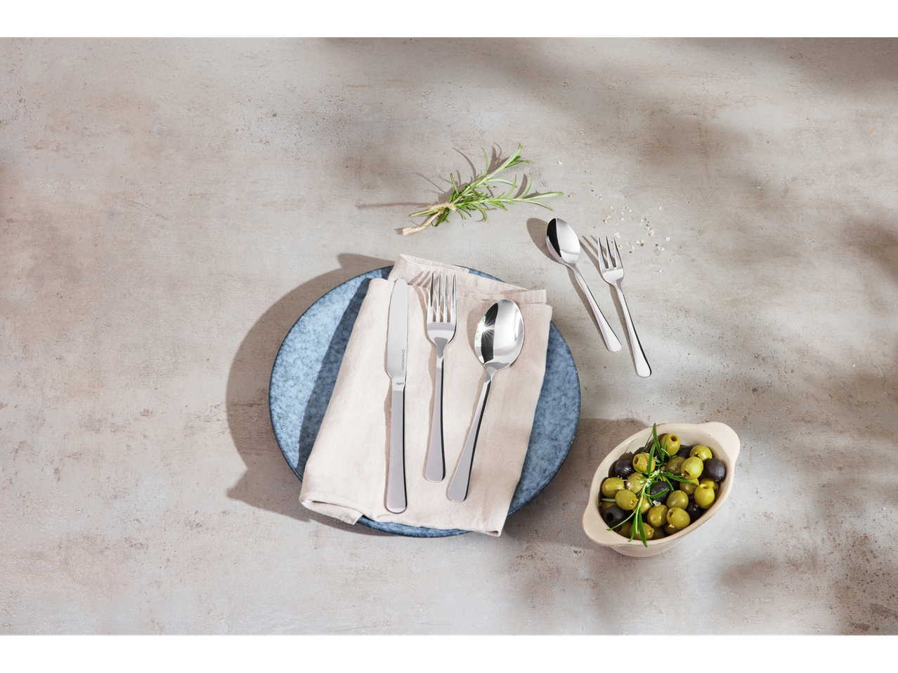 Ensemble de couverts élégants en acier inoxydable, servi sur une assiette avec une collation d'olives.