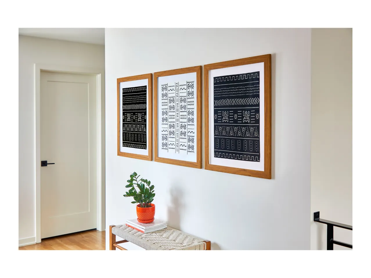 Three framed black and white tribal art prints hanging on a wall above a bench.