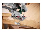 A person wearing gloves uses a circular saw with a dust extraction hose to cut a wooden board.