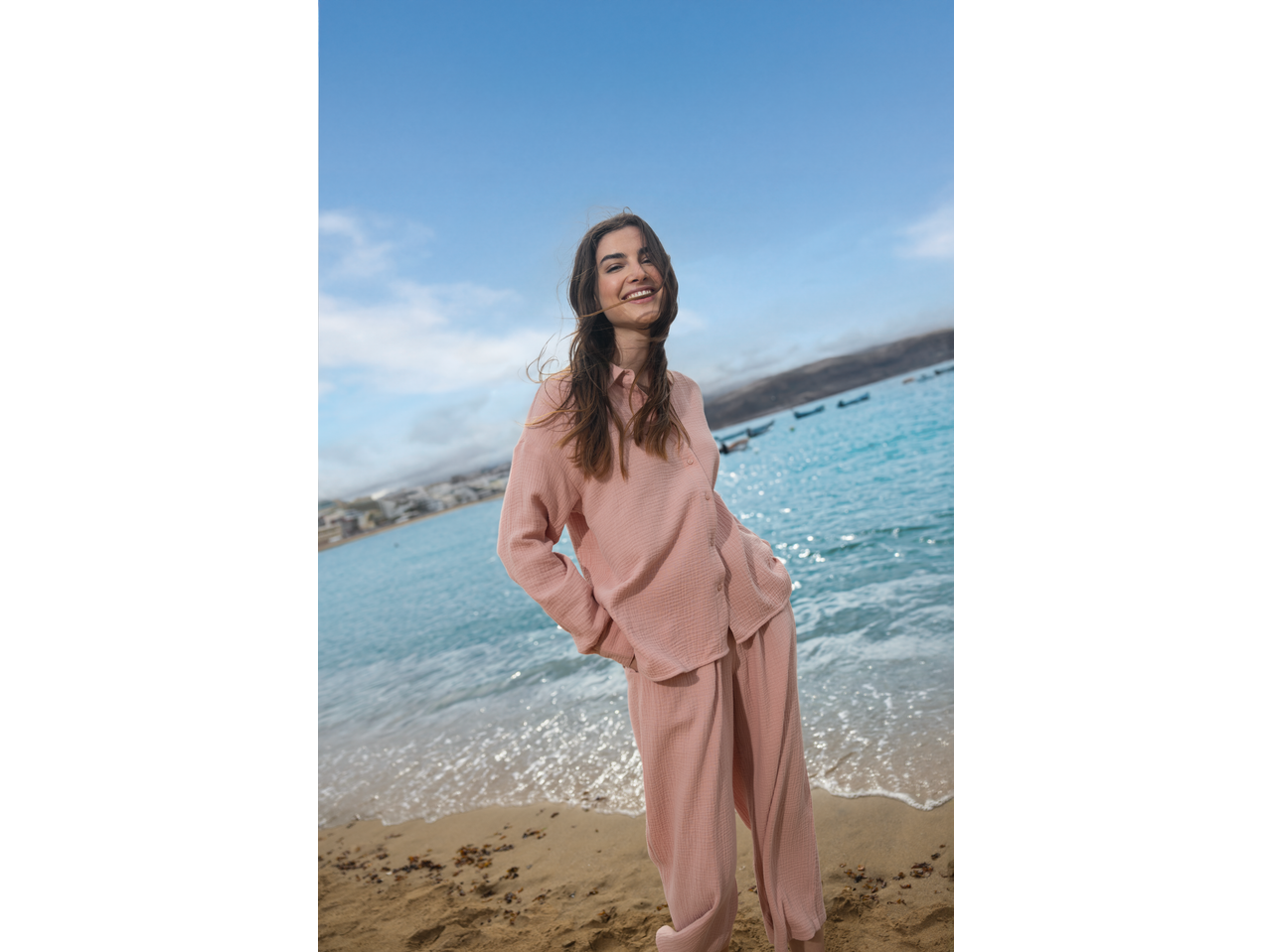 Χαμογελαστή γυναίκα με πουκάμισο και παντελόνι μουσελίνας ESMARA, στην παραλία.