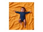 A baby in a navy blue bodysuit lying on a textured orange blanket.