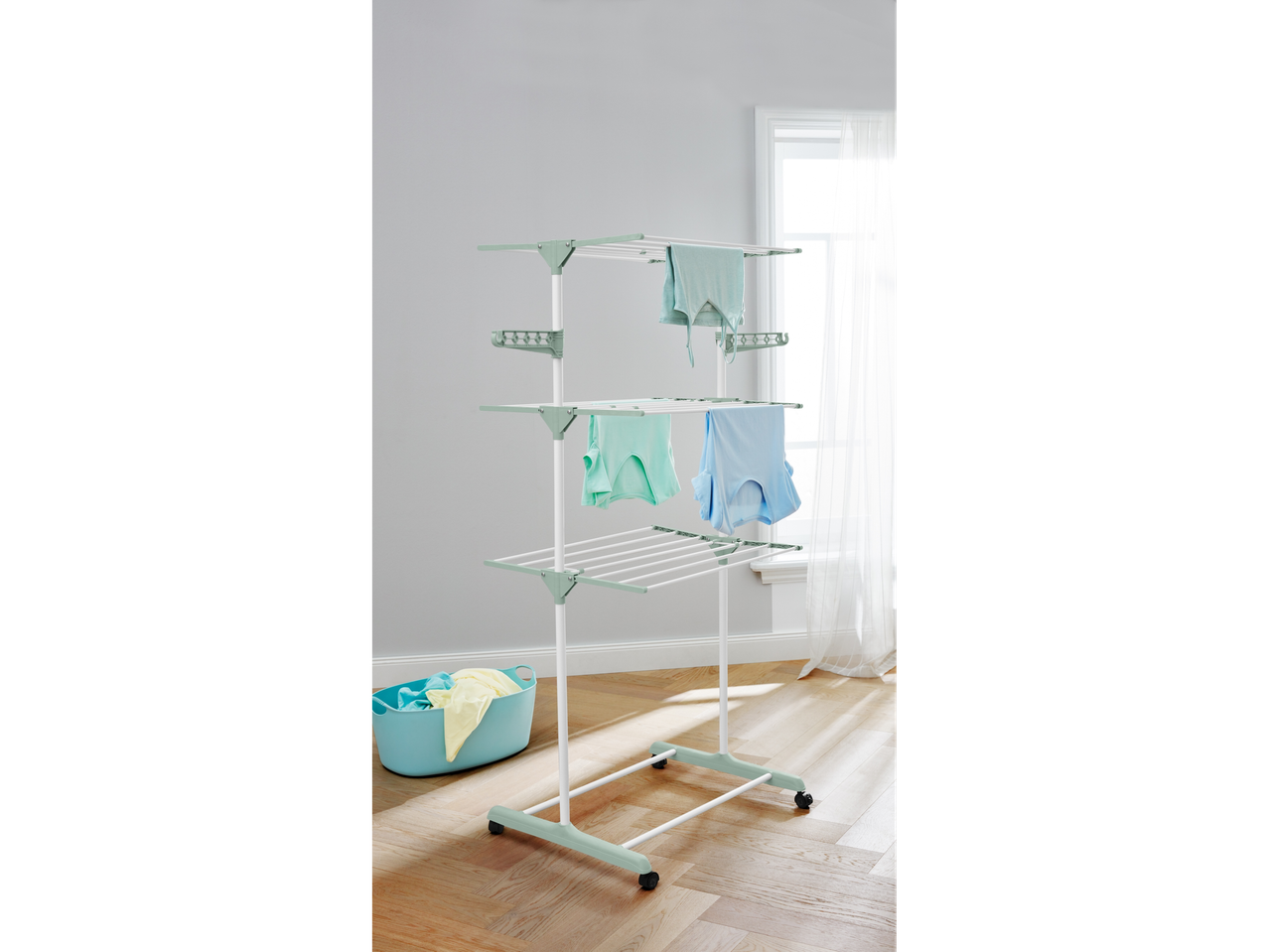 A three-tiered laundry drying rack with clothes hanging and a laundry basket nearby.