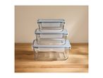 Three rectangular glass food storage containers with blue lids, stacked on a wooden surface.
