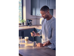 Man frothing milk with a handheld frother in a kitchen, with a latte nearby.