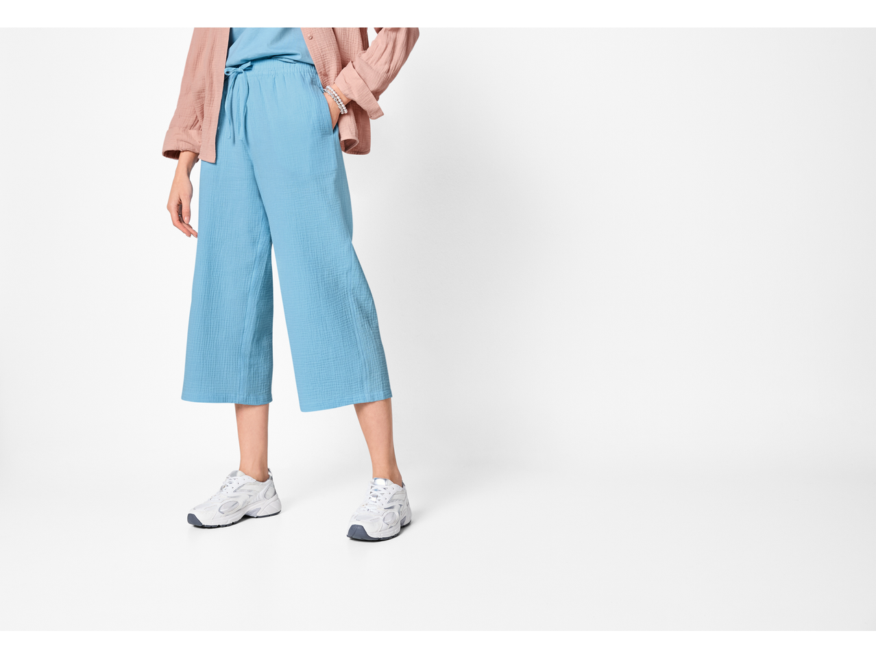 Pantaloni de muselină ESMARA pentru femei, de culoare albastru deschis, combinați cu o cămașă roz și adidași albi.