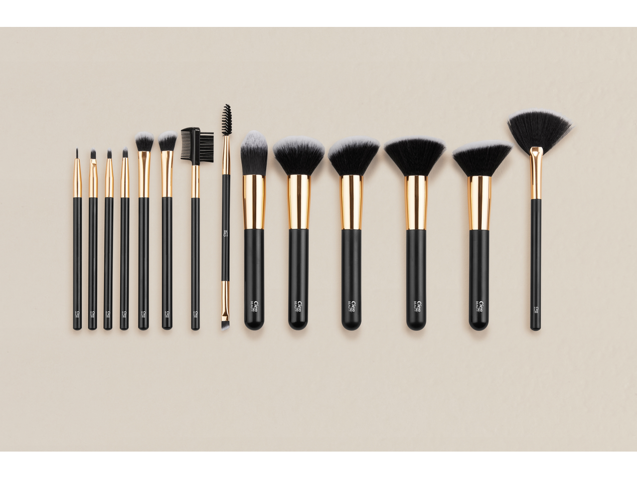 A collection of black and gold makeup brushes of various sizes and shapes, neatly arranged on a light background.