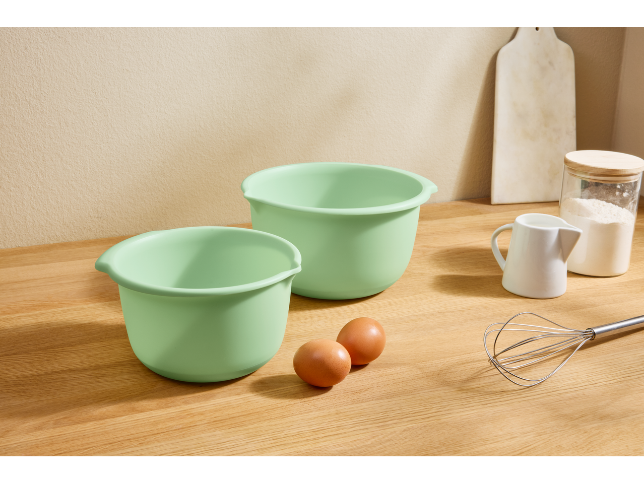 Dve zelene Zenker® posude za mešanje, jaja, brašno i žica na drvenoj radnoj ploči.