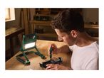 Man repairing a camera with a screwdriver, illuminated by a work light on a wooden table.