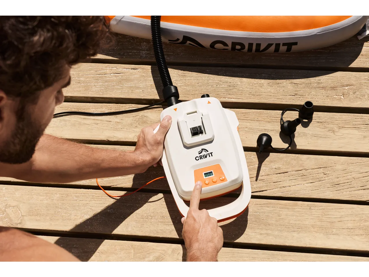 A man inflates a CRIVIT Inflatable All-Round Stand Up Paddle Board with an electric pump.