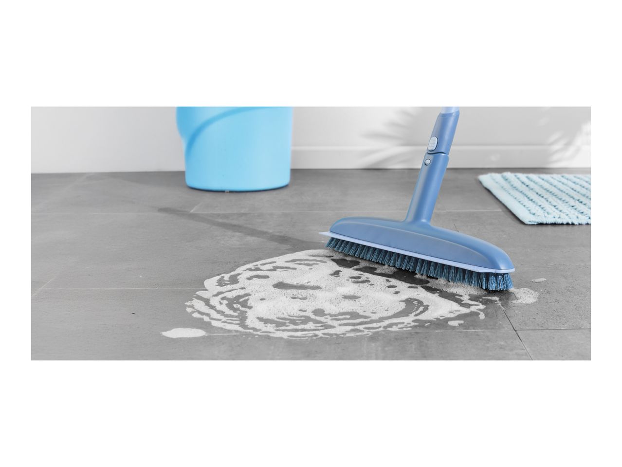 Blue floor brush cleaning a tiled floor with soapy water, a bucket, and a mat in the background.