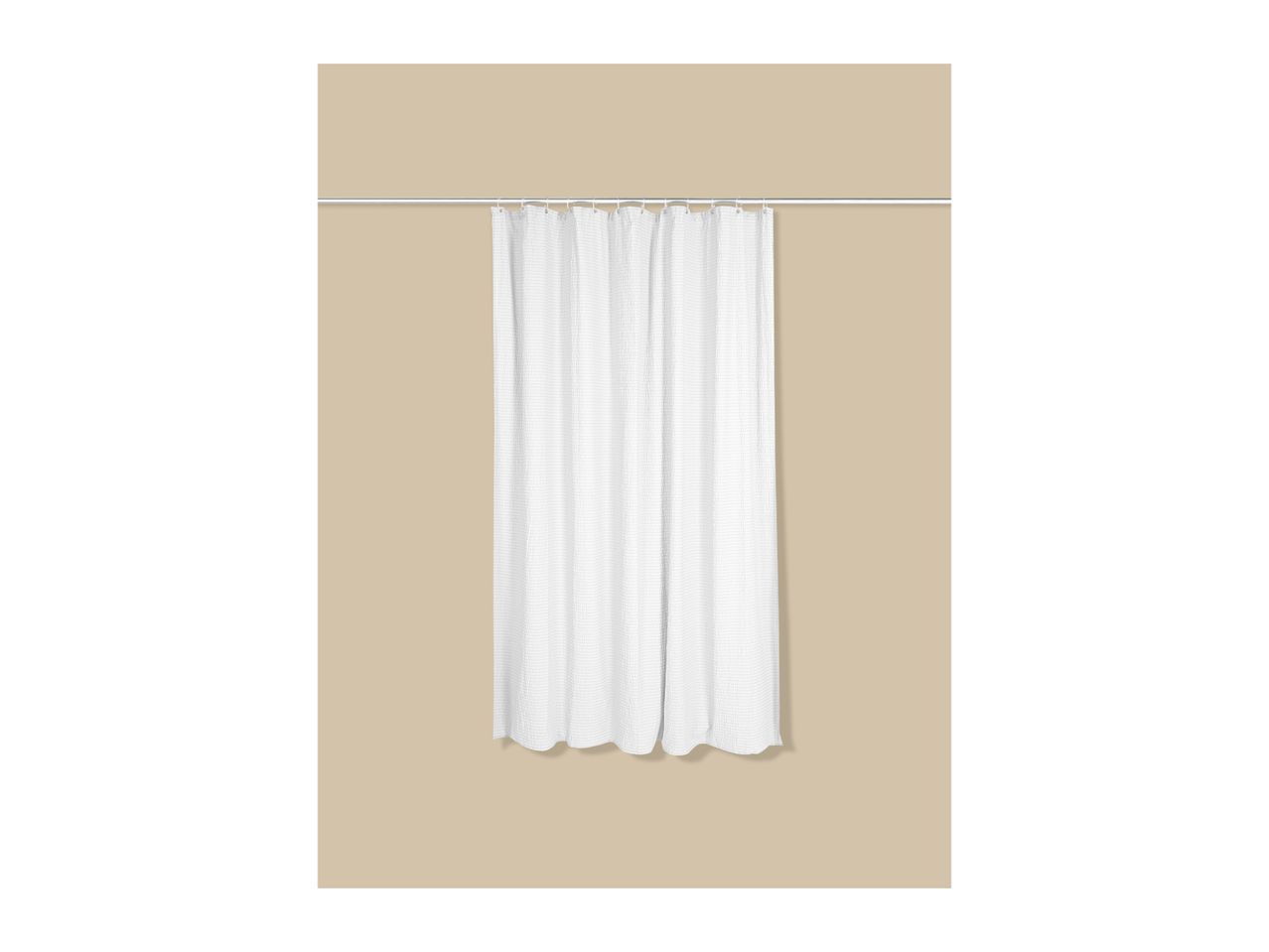 White shower curtain with a textured pattern hanging on a silver rod against a beige wall.