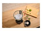 Blender with ice cubes, limes, raspberries, and a drink on a wooden kitchen counter.