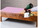 Uma pessoa usa um pulverizador de tinta Parkside para pintar uma velha mesa de madeira de rosa.