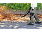 Ένα άτομο χρησιμοποιεί φυσητήρα φύλλων Parkside για να καθαρίσει τα φθινοπωρινά φύλλα από έναν δρόμο με πλακόστρωτο.