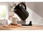 Black SilverCrest kettle pouring hot water into a mug on a wooden table.