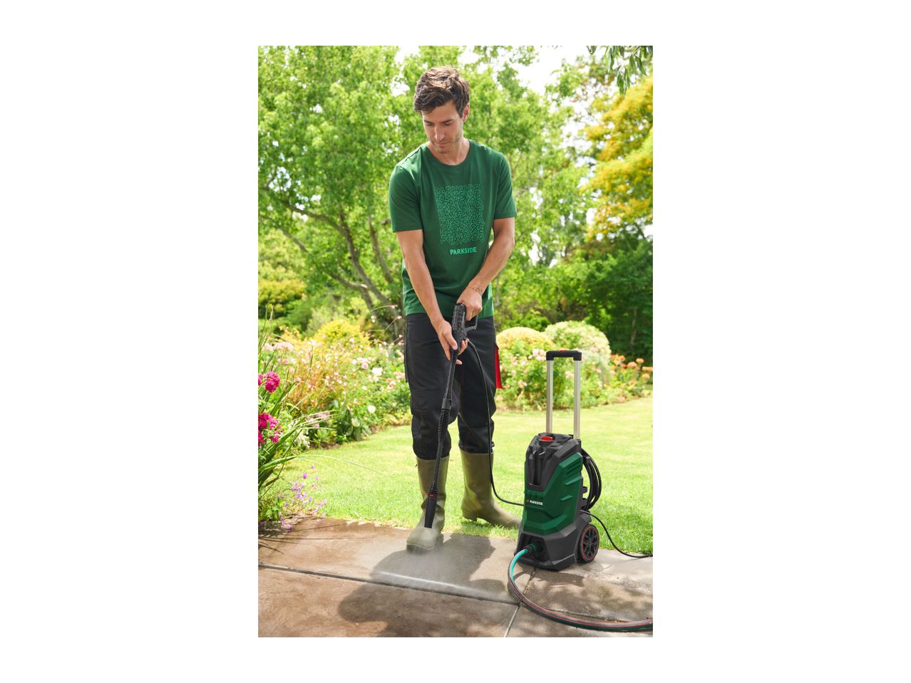 Man in green t-shirt and boots pressure washing a patio with a pressure washer.
