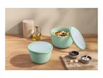Two mint green food storage containers, one filled with pasta salad, on a wooden counter.