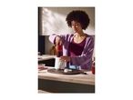 A woman using a compact white blender to make a berry smoothie in a kitchen.