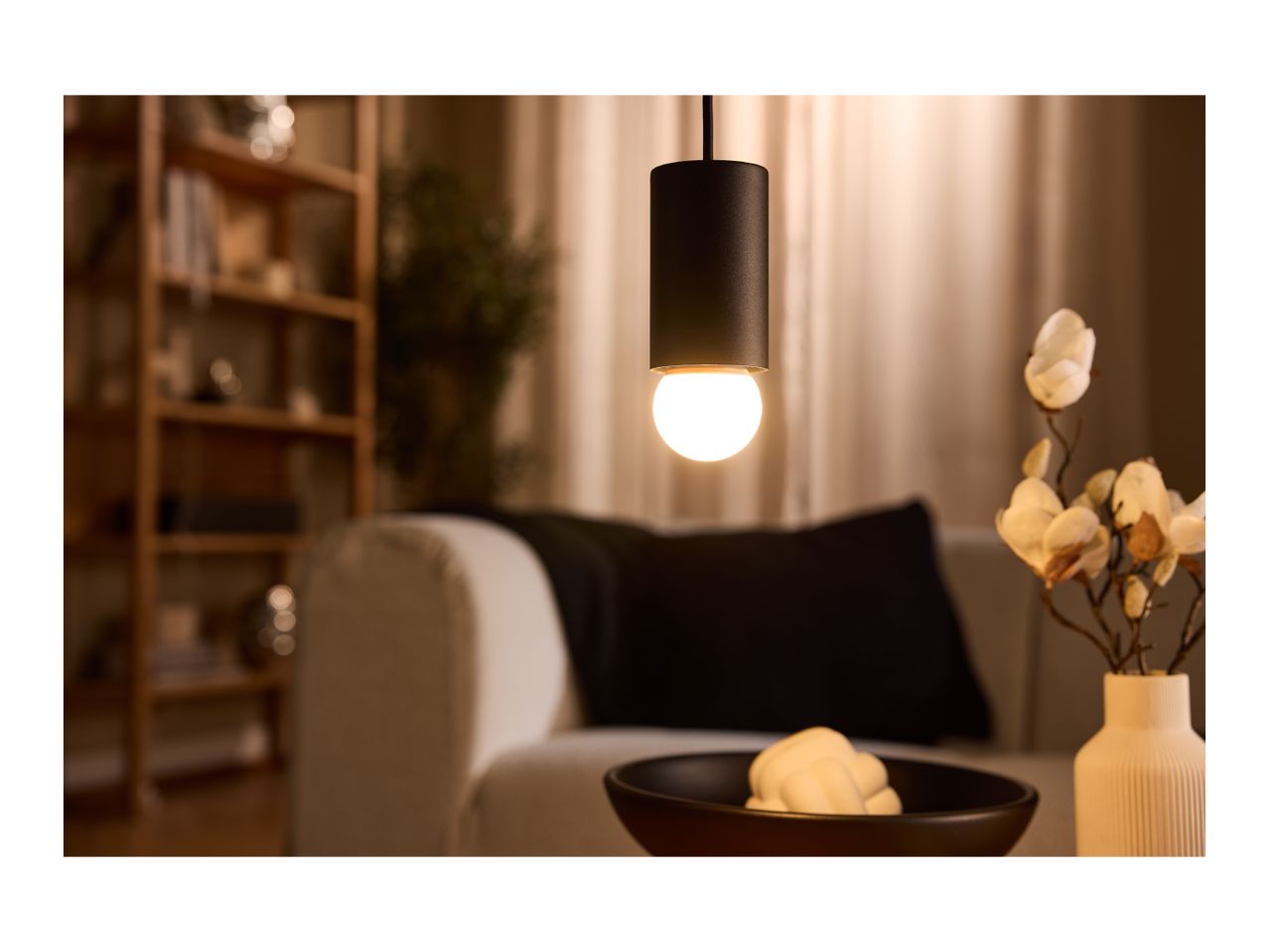 Warmly lit living room with a hanging pendant light, sofa, and decorative vase.