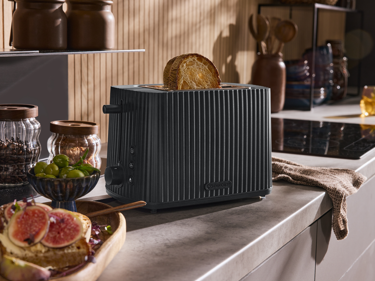Черен тостер с филия хляб в модерна кухня с дървени акценти и храна.
