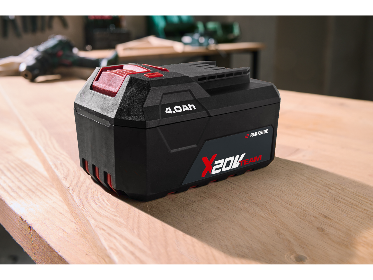 Parkside X 20 V Team 4.0 Ah baterija na drvenom stolu, s mutnim alatima u pozadini.
