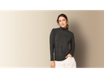 Woman in a dark gray turtleneck and white pants, hand in pocket.