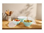 Mint green bowls with food and lids on a wooden counter, with kitchen utensils in a holder.