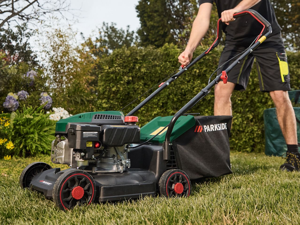 A person uses a Masport petrol lawn mower to cut grass.