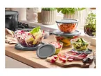 Glass food storage containers with grey lids, filled with fresh vegetables on a kitchen counter.