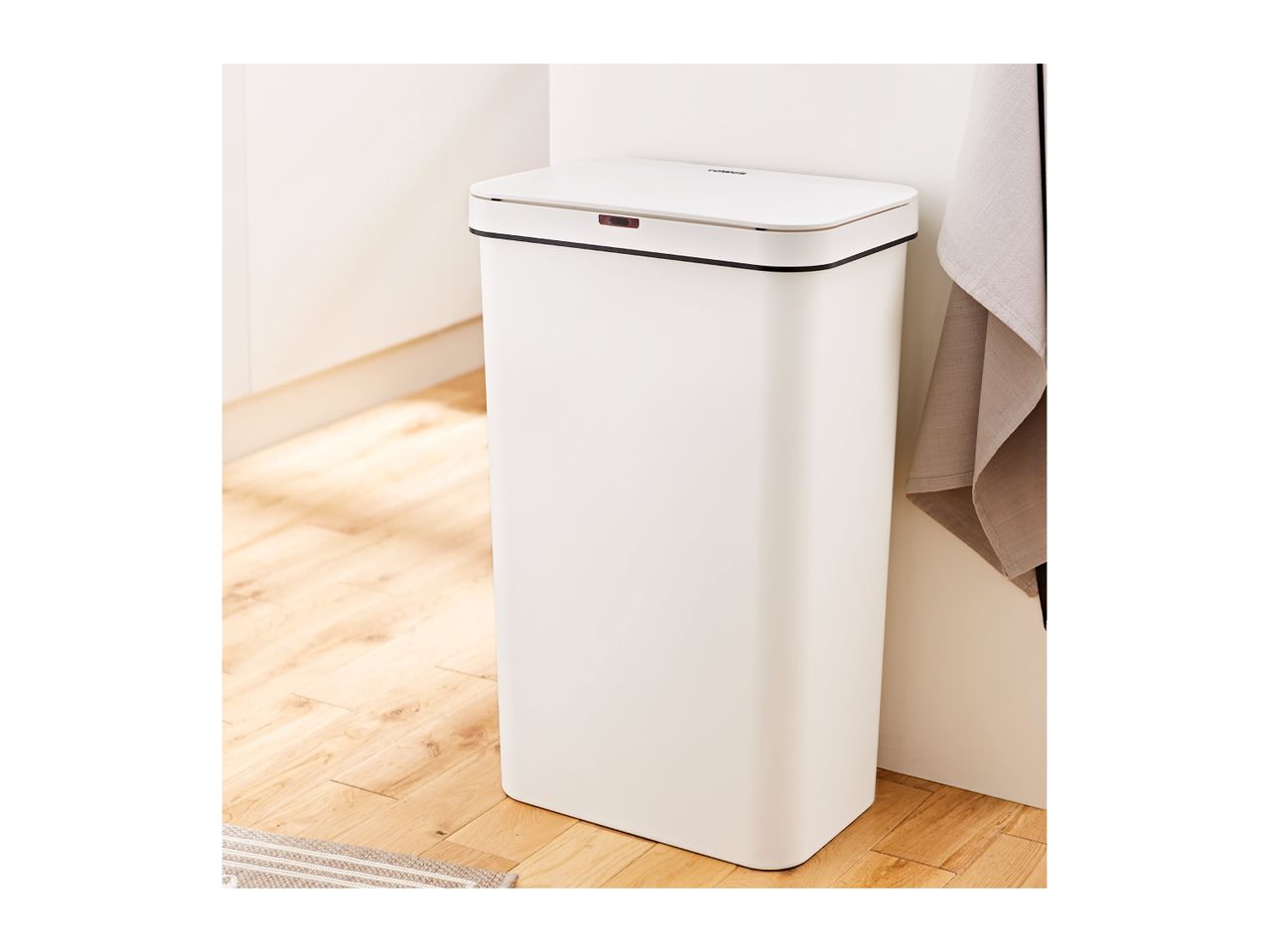 A white, touch-free TOMMEER trash can stands on a light wood floor.