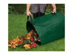 A person emptying a green garden waste bag filled with colorful autumn leaves onto a lawn.