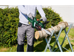 Man cutting a wooden log with an electric chainsaw on a sawhorse in the garden.