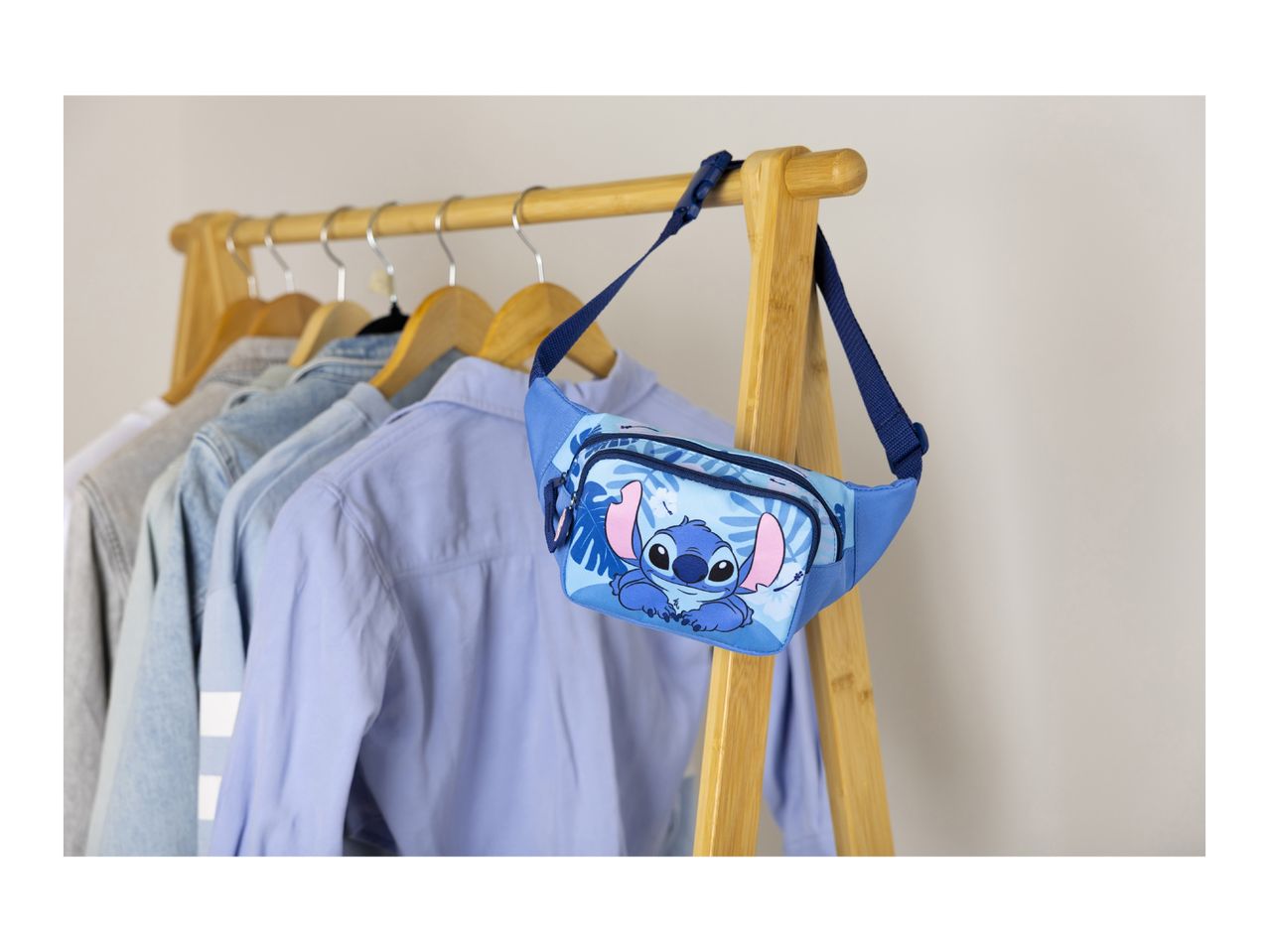 Blue fanny pack with a cartoon character and tropical leaves, hanging on a wooden clothes rack.