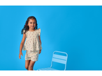 Young girl in a floral top and shorts set, standing next to a blue chair.