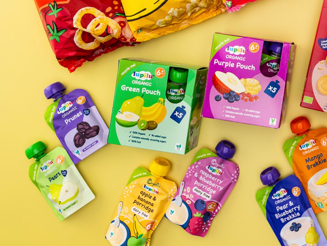 A variety of Lupilu organic baby food pouches and boxes, including fruit purees and porridges, on a yellow background.
