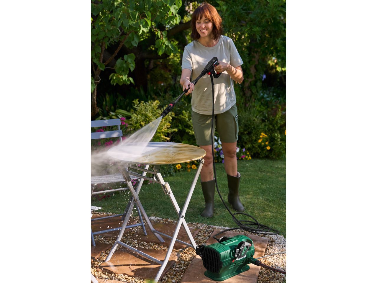 Woman pressure washing a dirty garden table with a compact pressure washer.