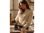 Femeie turnând boabe de cafea într-o râșniță de cafea SILVERCREST® pe o masă de mic dejun.