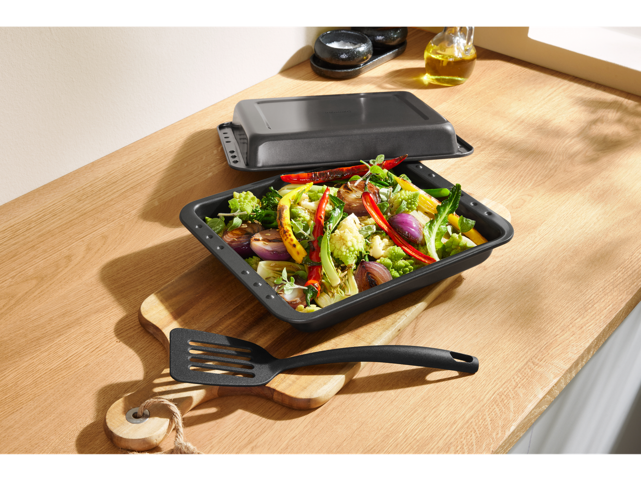 Silvercrest® Plats à four: тава за печене със зеленчуци и шпатула върху дървена дъска.