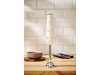 Cream immersion blender on a wooden counter with a bowl of soup and cutlery.