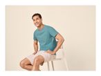 Man in a teal t-shirt and light shorts, sitting on a chair and smiling.