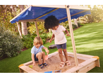 Two children playing in a wooden sandbox with a blue canopy, surrounded by green grass.