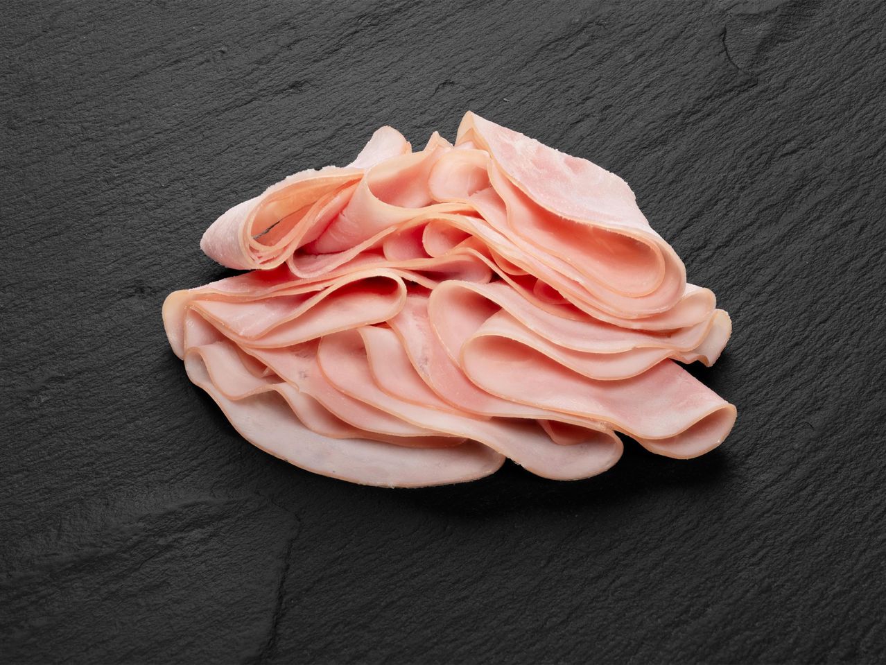 Szeletelt sonka halomban, fekete háttér előtt.